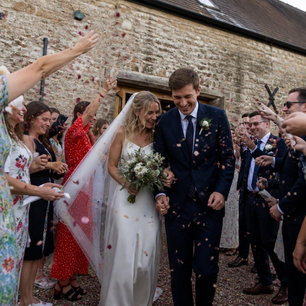 Newlywed couple walking through confetti thrown by guests outside the venue